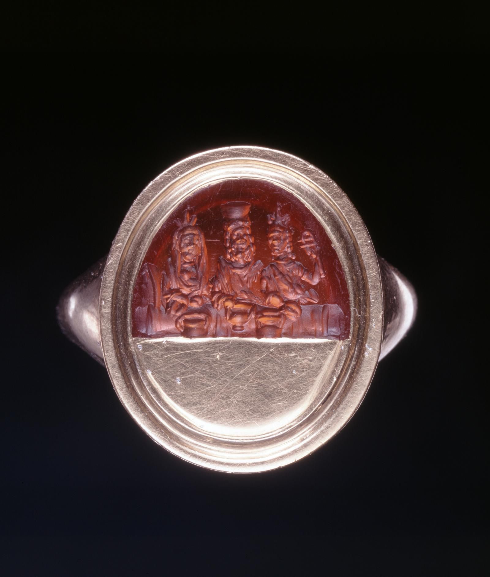 Roman sard intaglio, engraved with the divine couple Serapis and Isis, and a female figure holding a sistrum (a ritual rattle), mounted on a modern gold setting, 1st-3rd Century AD.